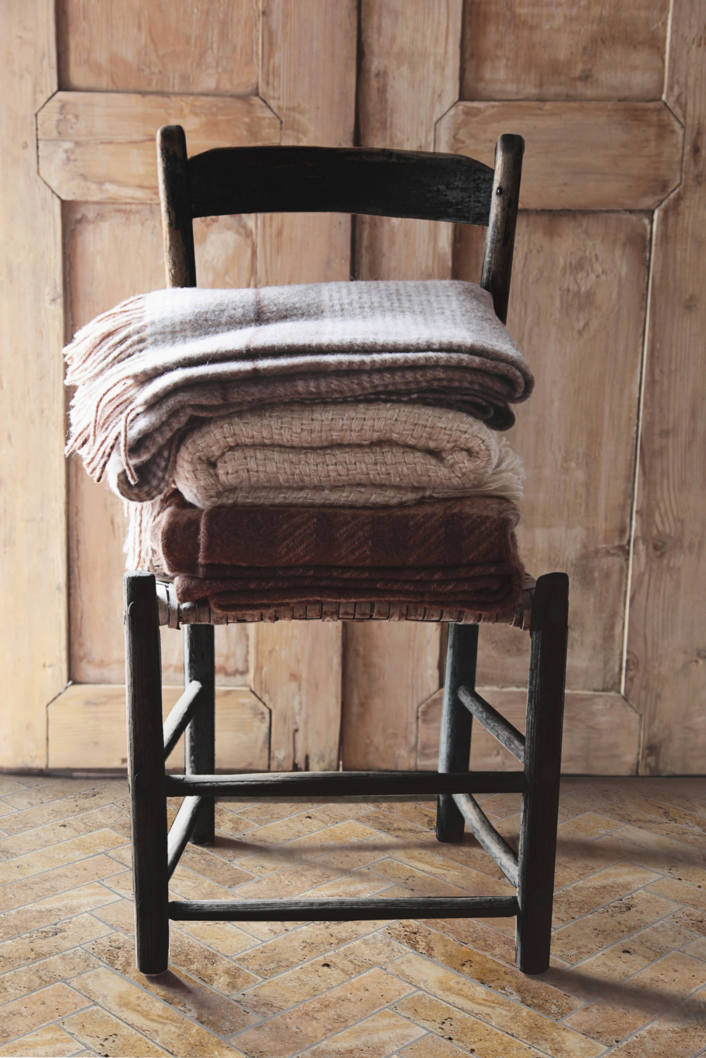 a stack of blankets on a wooden chair standing on a tile floor.