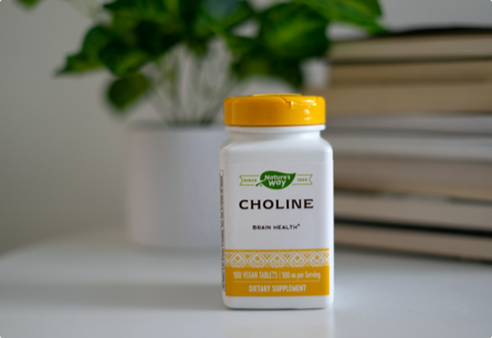 A bottle of Choline sitting on a table in front of a green, leafy plant.