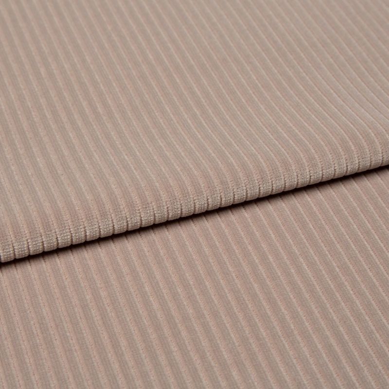 Ribbed beige corduroy fabric, folded into two layered panels showing parallel ridges, photographed close-up on a neutral surface with soft, even studio lighting.