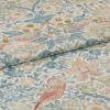 Folded printed fabric with pastel floral and bird motif and visible linen texture lies folded across itself, close-up on a flat surface in soft, diffuse light.
