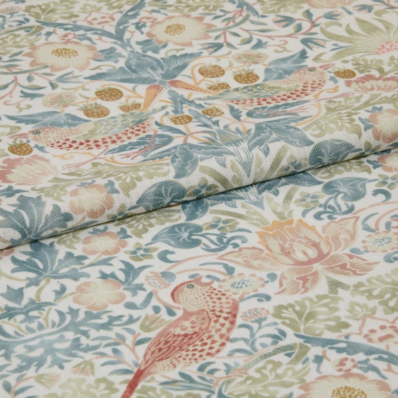 Folded printed fabric with pastel floral and bird motif and visible linen texture lies folded across itself, close-up on a flat surface in soft, diffuse light.