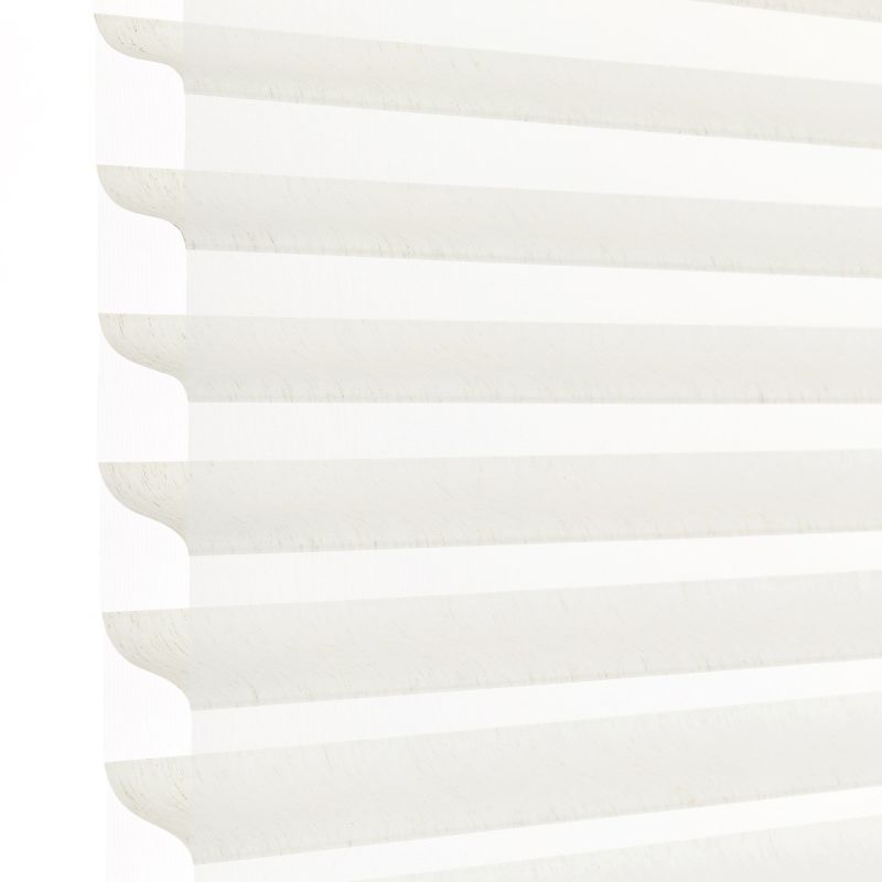 White horizontal pleated cellular blind with scalloped edges, fully lowered and closed, filtering bright daylight; close-up view showing soft shadowed ridges against a pale background.