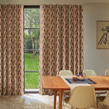 Patterned floor-to-ceiling pleated curtains, pink geometric print, drawn across a tall multi-pane window, filtering daylight into a dining room with a wooden table, chairs, and a grassy garden view.