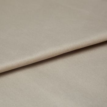 Beige velvet fabric, folded diagonally with a soft nap and slight sheen; overlapping edge creates a crease, shown in a close-up under diffuse neutral lighting on a flat surface.