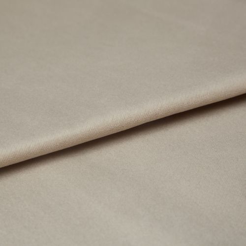Beige velvet fabric, folded diagonally with a soft nap and slight sheen; overlapping edge creates a crease, shown in a close-up under diffuse neutral lighting on a flat surface.