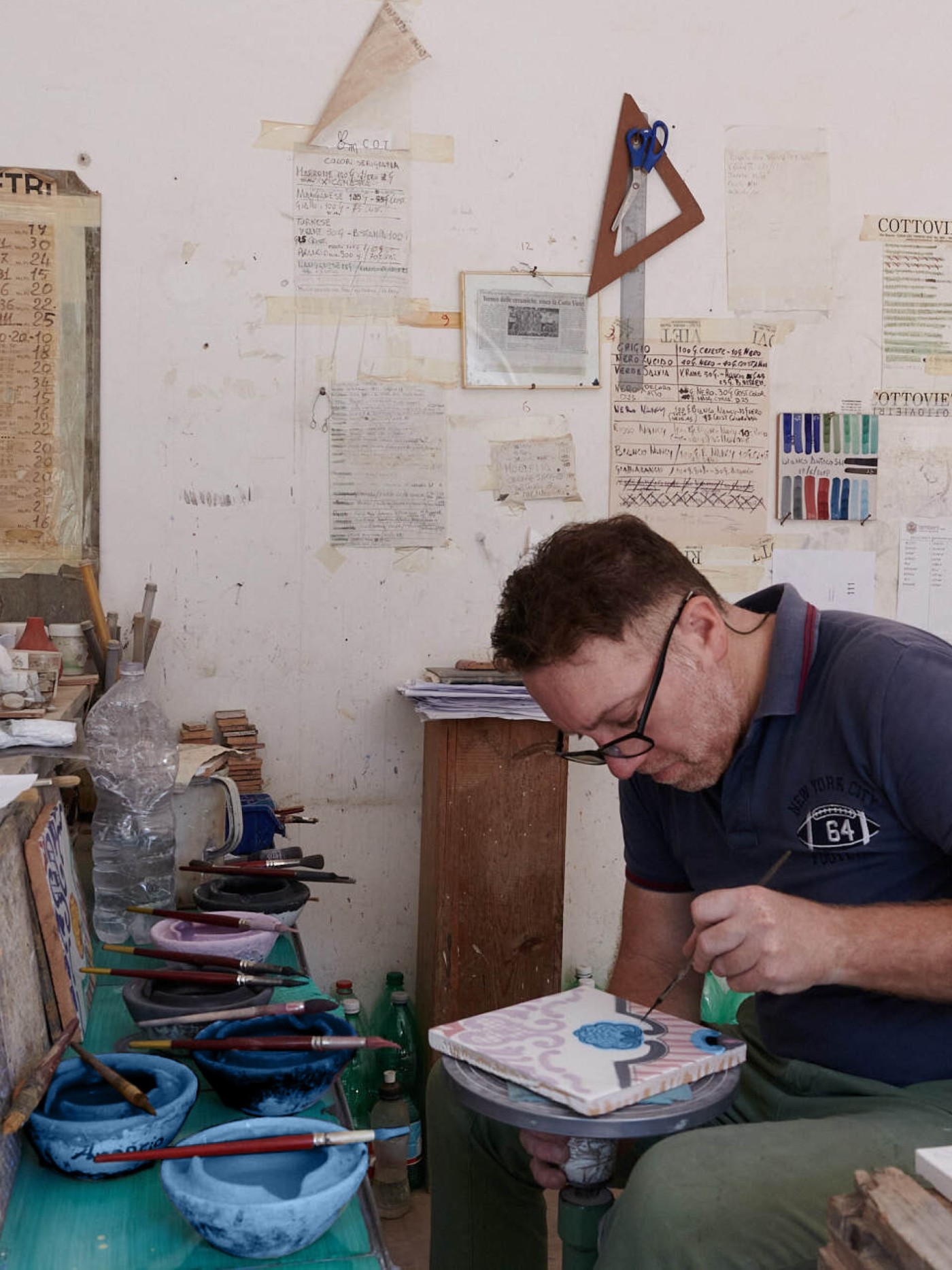 a man hand painting a tile in a workshop.