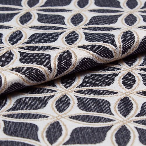 Jacquard upholstery fabric with cream and tan interlocking petal lattice on a black textured ground, folded across itself, showing raised embroidered weave; close-up, softly lit studio setting.