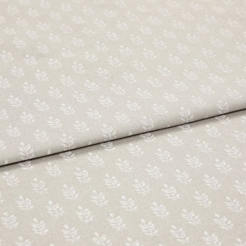 Beige cotton fabric with small white leaf motif, folded once to reveal overlapping layers; lying flat on a neutral surface under soft, even studio lighting for a close-up textile display.