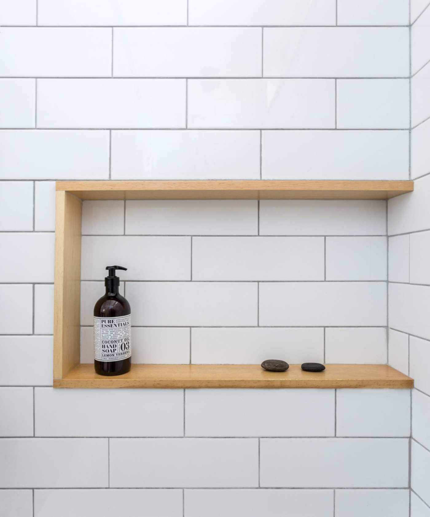 a white tiled shower with a wooden shelf.