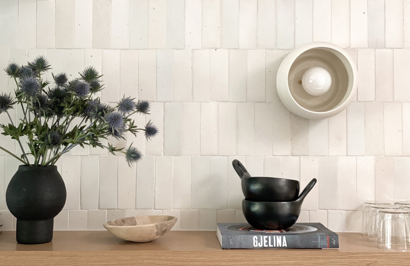 a counter with some bowls, a book, and a potted plant in front of a white tiled wall.