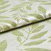 Folded jacquard fabric with raised pale-green leaf pattern on a cream background; fabric overlaps and rests, shown in a close-up view with soft directional lighting revealing its texture.