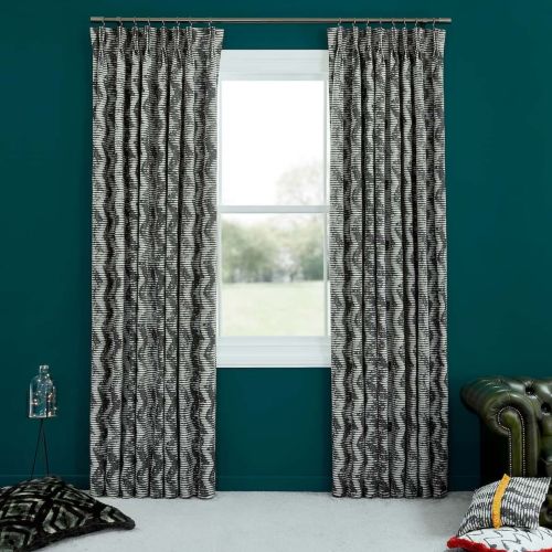 Black-and-white wavy-striped pleated curtain panels, hung on a metal rod and parted, framing the central window and admitting daylight into a teal-walled room with cushions and a green leather armchair.