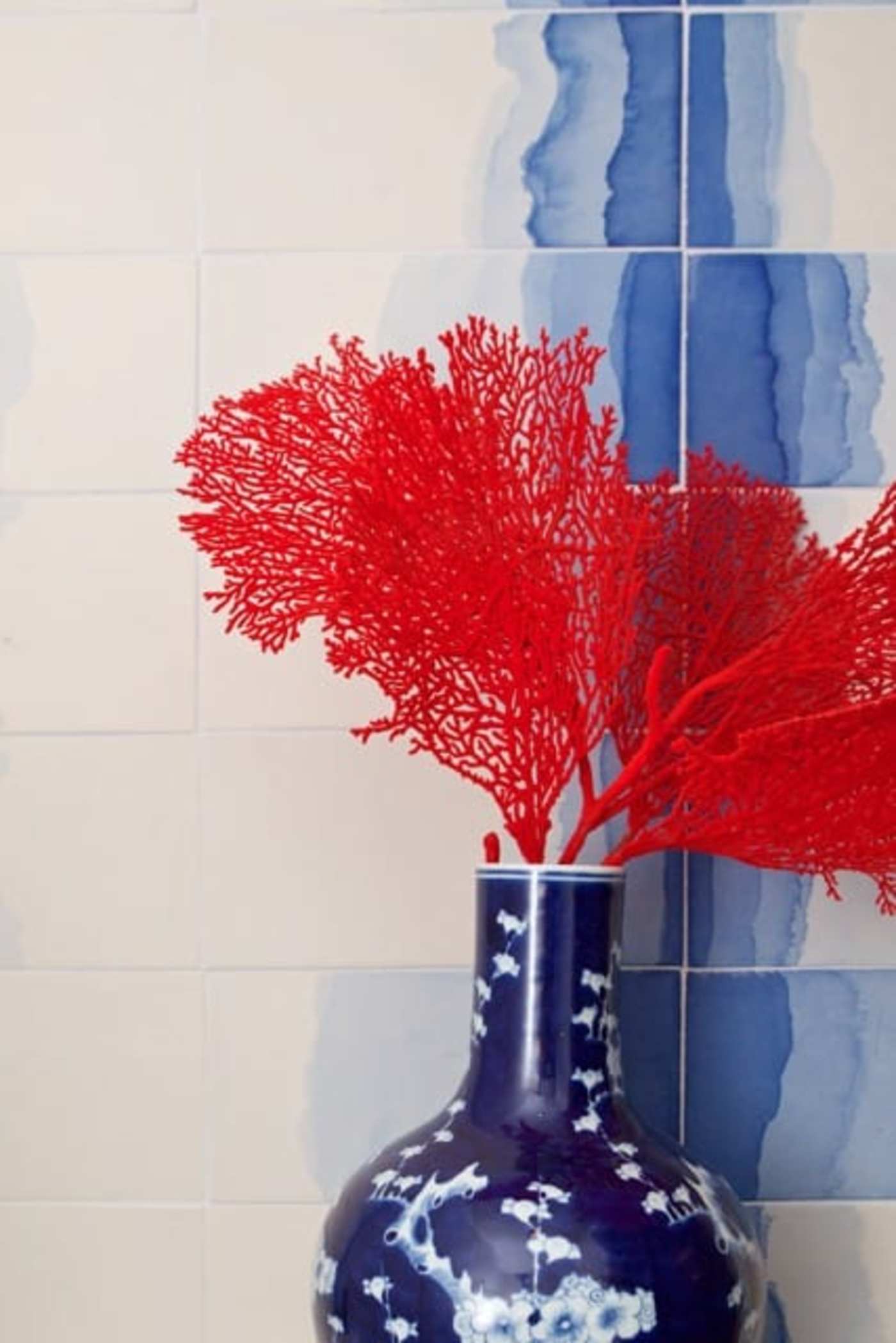 a vase with red and blue flowers in front of a white and blue tiled wall.