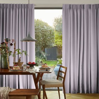 Floor-length pleated lavender curtains, drawn slightly apart to reveal a central opening, softly filtering daylight; dining table with pancakes and pendant lamp in foreground, backyard garden visible beyond.