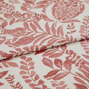Cream fabric printed with terracotta botanical and pomegranate motifs, folded and overlapped to show pattern repeat, close-up on a flat surface under soft, even studio lighting.