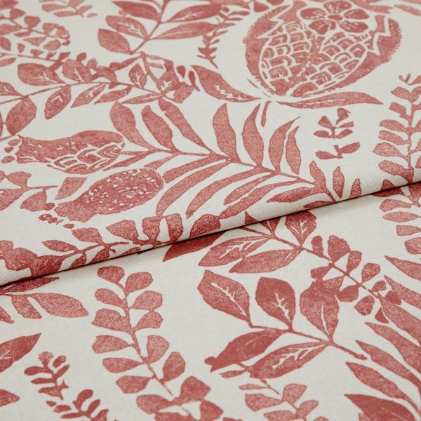 Cream fabric printed with terracotta botanical and pomegranate motifs, folded and overlapped to show pattern repeat, close-up on a flat surface under soft, even studio lighting.