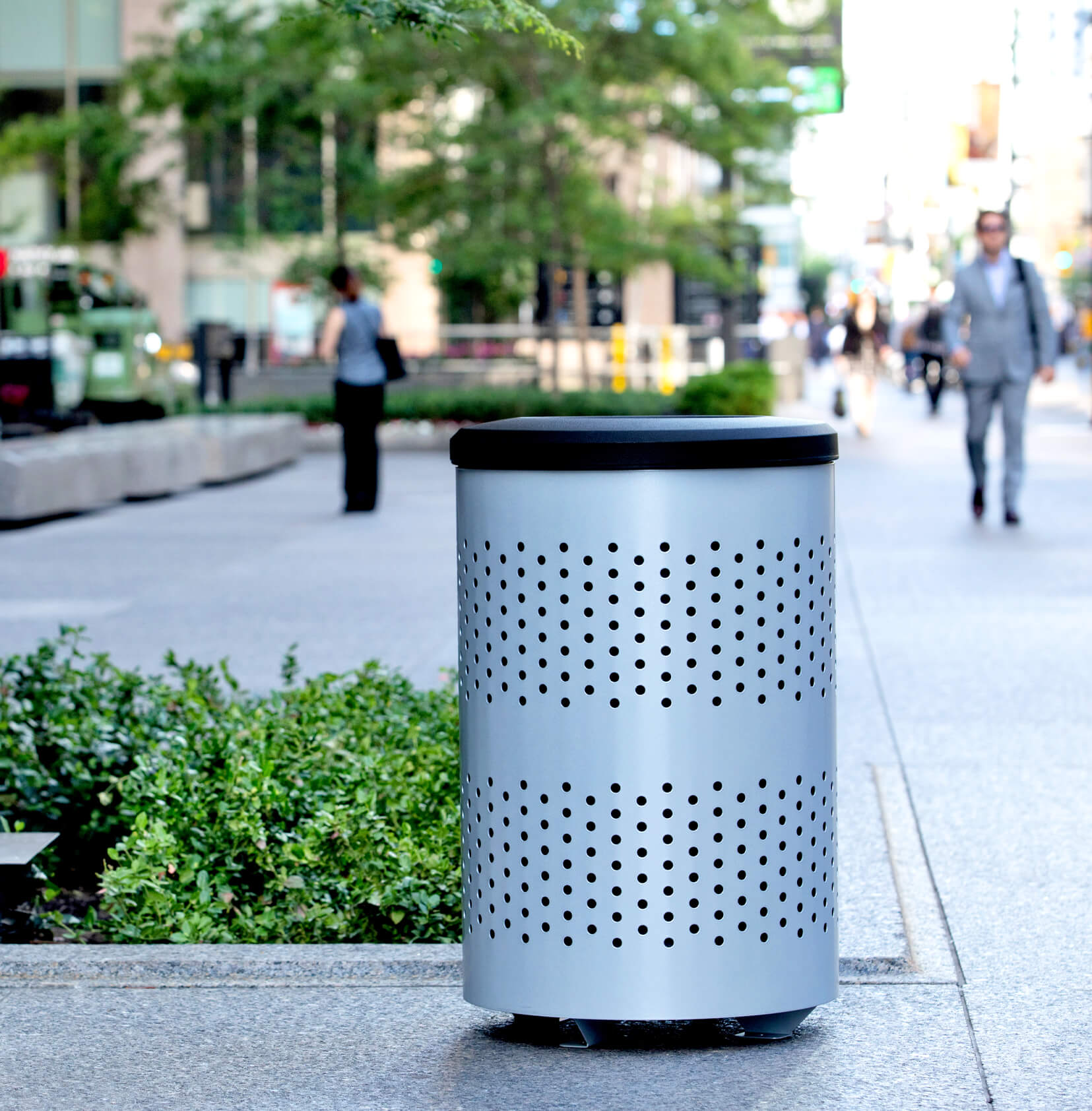 outdoor metal waste container with a silver body and black plastic lid in front of a downtown office building