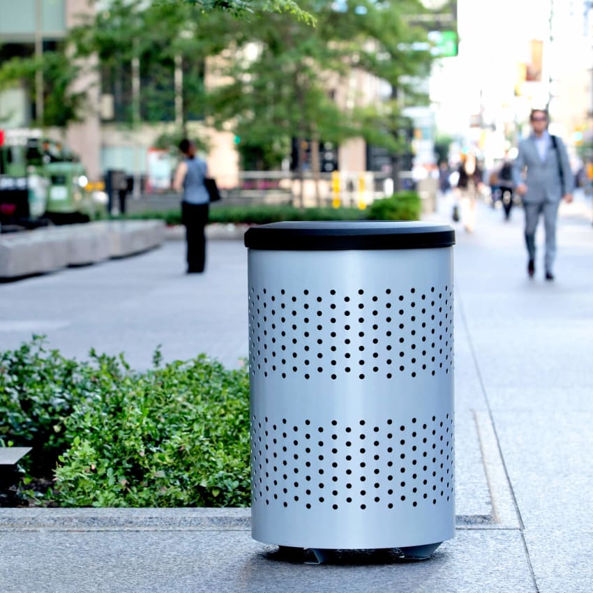 outdoor metal waste container with a silver body and black plastic lid in front of a downtown office building
