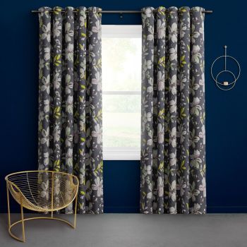 Floor-length grommet-top floral curtains, dark gray with white and lime blossoms, parted on a rod to filter daylight through a central window; navy room with gold chair and circular sconce.