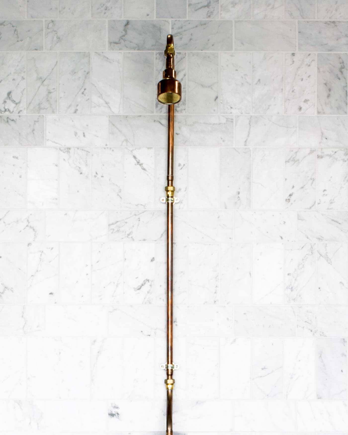 a brass shower head on a white marble tile wall.