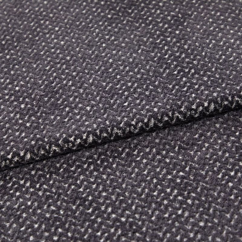Folded dark gray woven fabric (small white flecked texture) — layered edge overlapping — close-up studio view highlighting soft pile and subtle zigzag pattern.