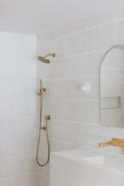 a white bathroom with a gold shower head and sink.