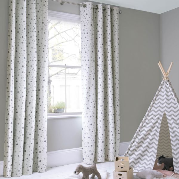 Grommet-top curtains with grey star print, hanging full-length on a metal rod, filtering bright daylight through the window into a softly lit grey nursery with a chevron teepee and toys.