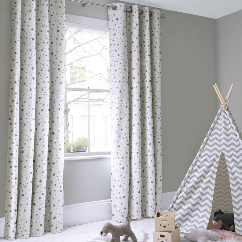 Grommet-top curtains with grey star print, hanging full-length on a metal rod, filtering bright daylight through the window into a softly lit grey nursery with a chevron teepee and toys.