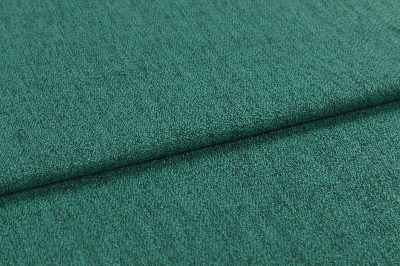 Teal-green textured upholstery fabric, close-up, showing short nap and subtle ribbing; folded horizontally with a visible overlap; photographed under soft, even lighting against an indistinct neutral background.