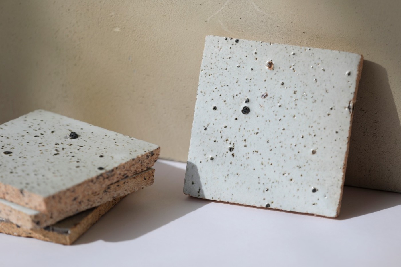 a set of square white tiles with speckles next to a brown wall.