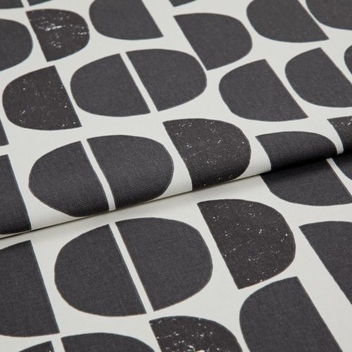 Folded printed fabric featuring large black semi-circles and vertical-split halves with subtle distressed speckling, folded over itself in a close-up studio shot with soft, even lighting.