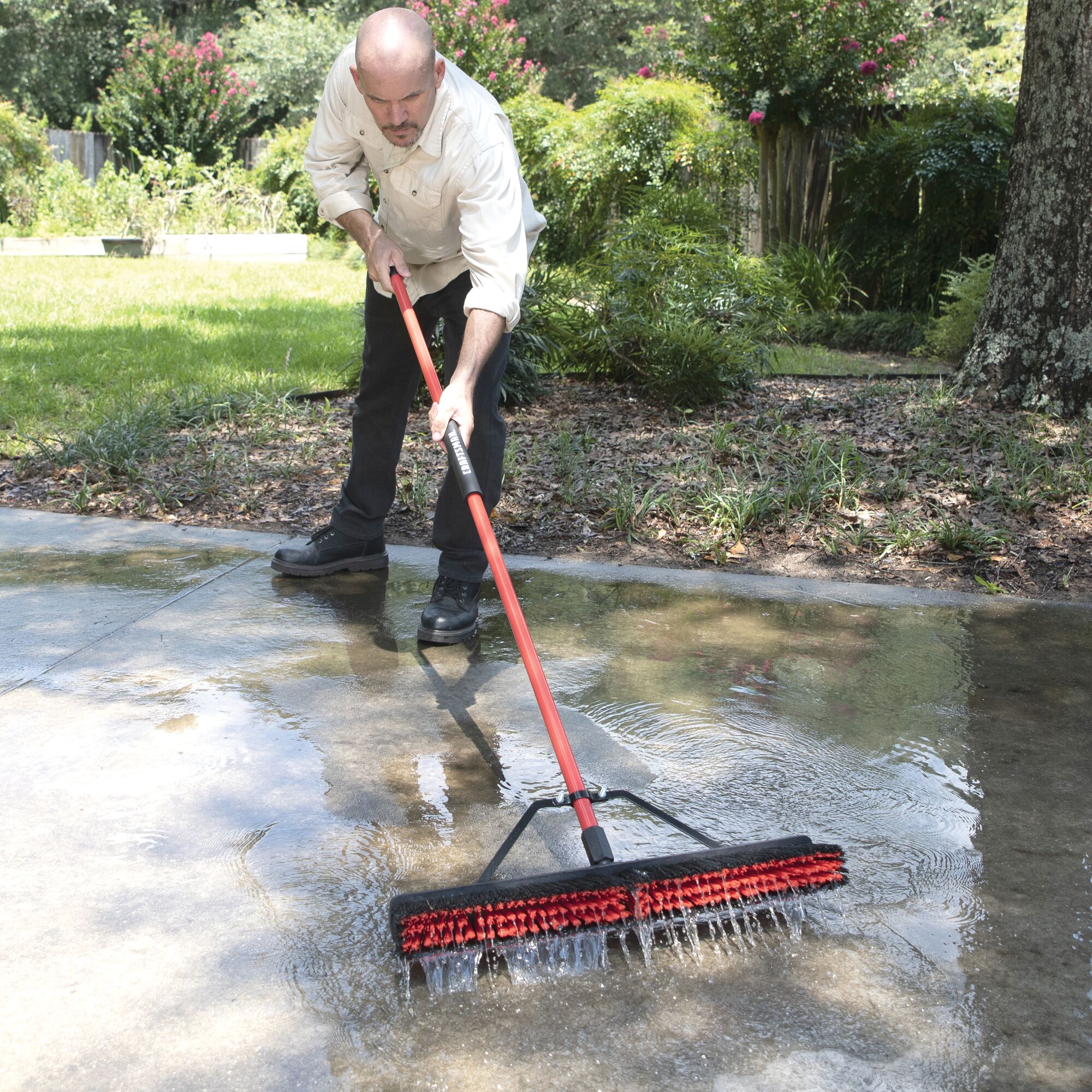 24 inch push broom with built in squeegee being used by a person to push water from the ground.