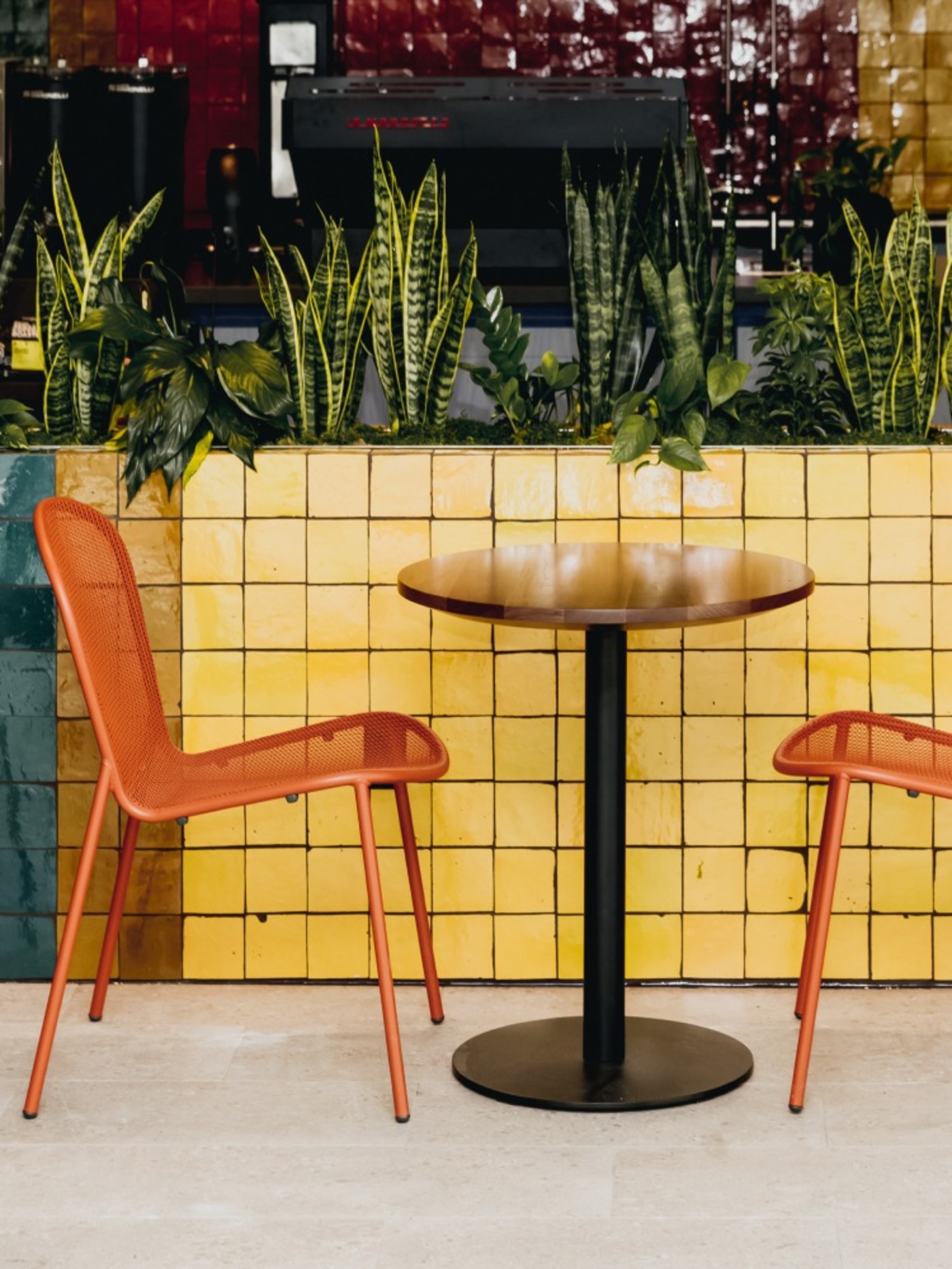 two orange chairs and a table in front of a yellow tiled wall.