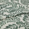 Botanical-printed cotton fabric, folded across the center revealing a layered edge, green leaf-and-fruit motifs on an off-white ground; close-up textile sample on a neutral surface under soft studio light.