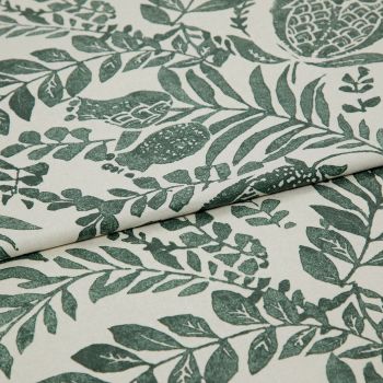 Botanical-printed cotton fabric, folded across the center revealing a layered edge, green leaf-and-fruit motifs on an off-white ground; close-up textile sample on a neutral surface under soft studio light.