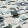 Folded geometric-print fabric sample with cream base and distressed blue, black and pale pink triangles and rectangles — draped flat in a close-up studio shot under soft even lighting.