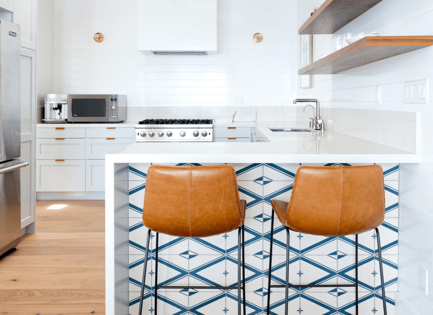 a white kitchen with brown stools and a blue and white tile counterside.