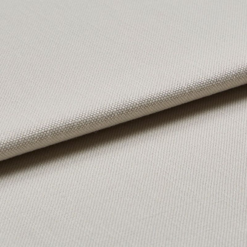 Beige woven fabric swatch folded diagonally, showing tight pebble-like texture; layered close-up under soft, neutral lighting, suggesting upholstery or curtain material.