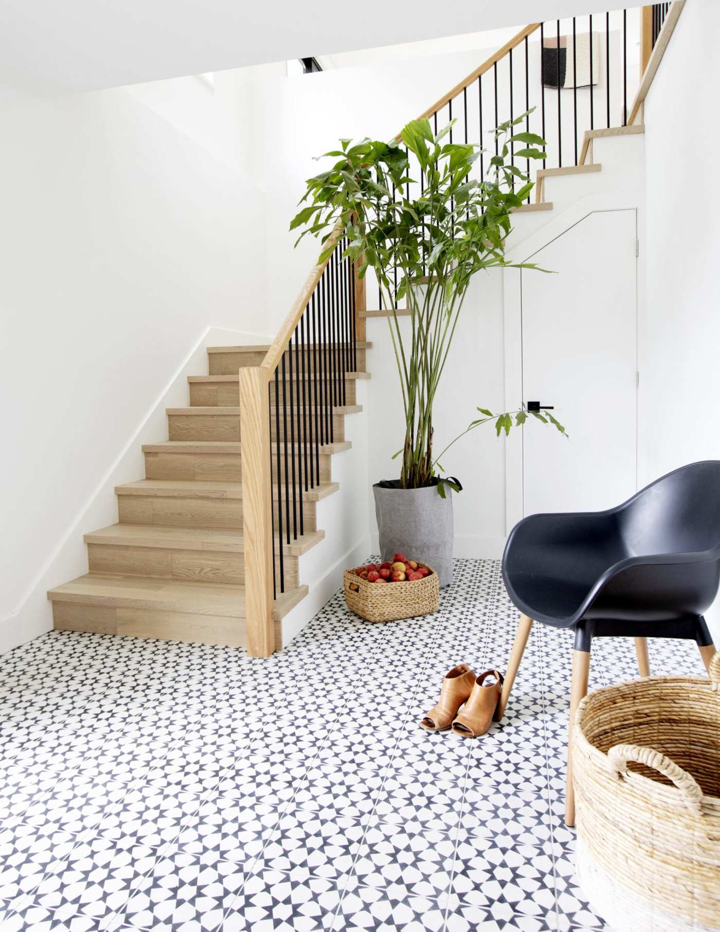 a black and white tiled entryway with a black chair and a potted plant.