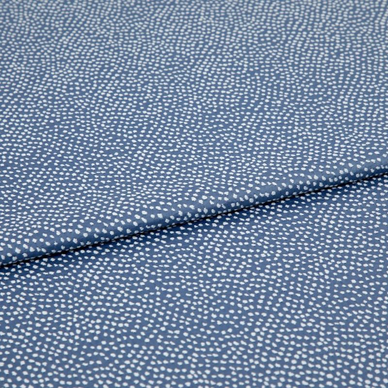 Blue fabric with dense, irregular white dot pattern, folded across the frame; lying flat and slightly overlapped, photographed close-up under soft, even studio lighting for a textile product shot.
