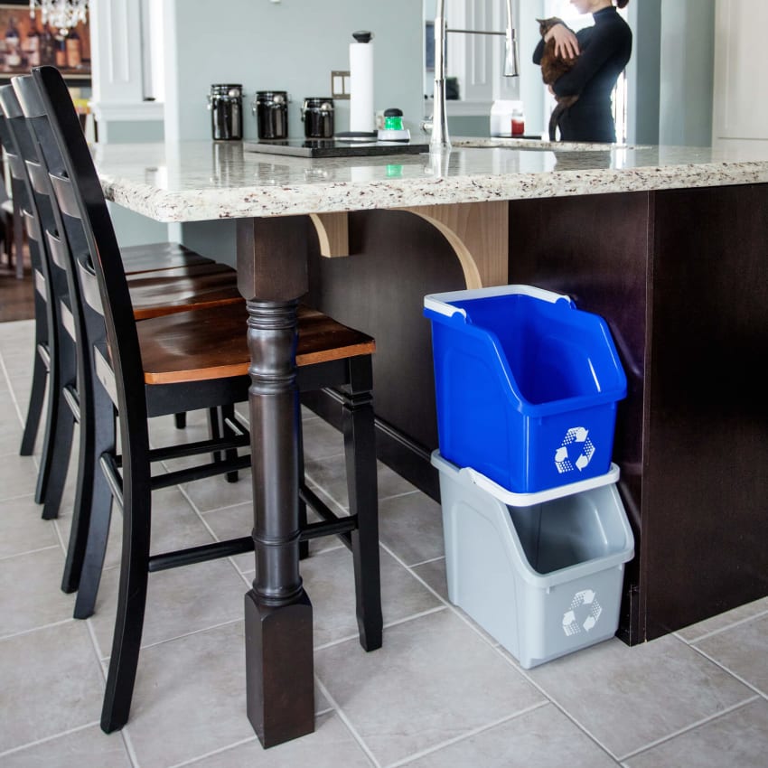 blue and grey stacking recycling bins under a kitchen island with a woman in the background holding a cat