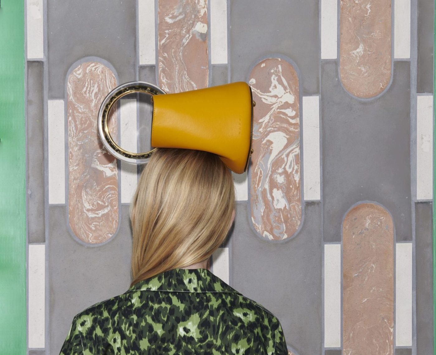 a woman in front of a tiled wall with a yellow handbag on her head.