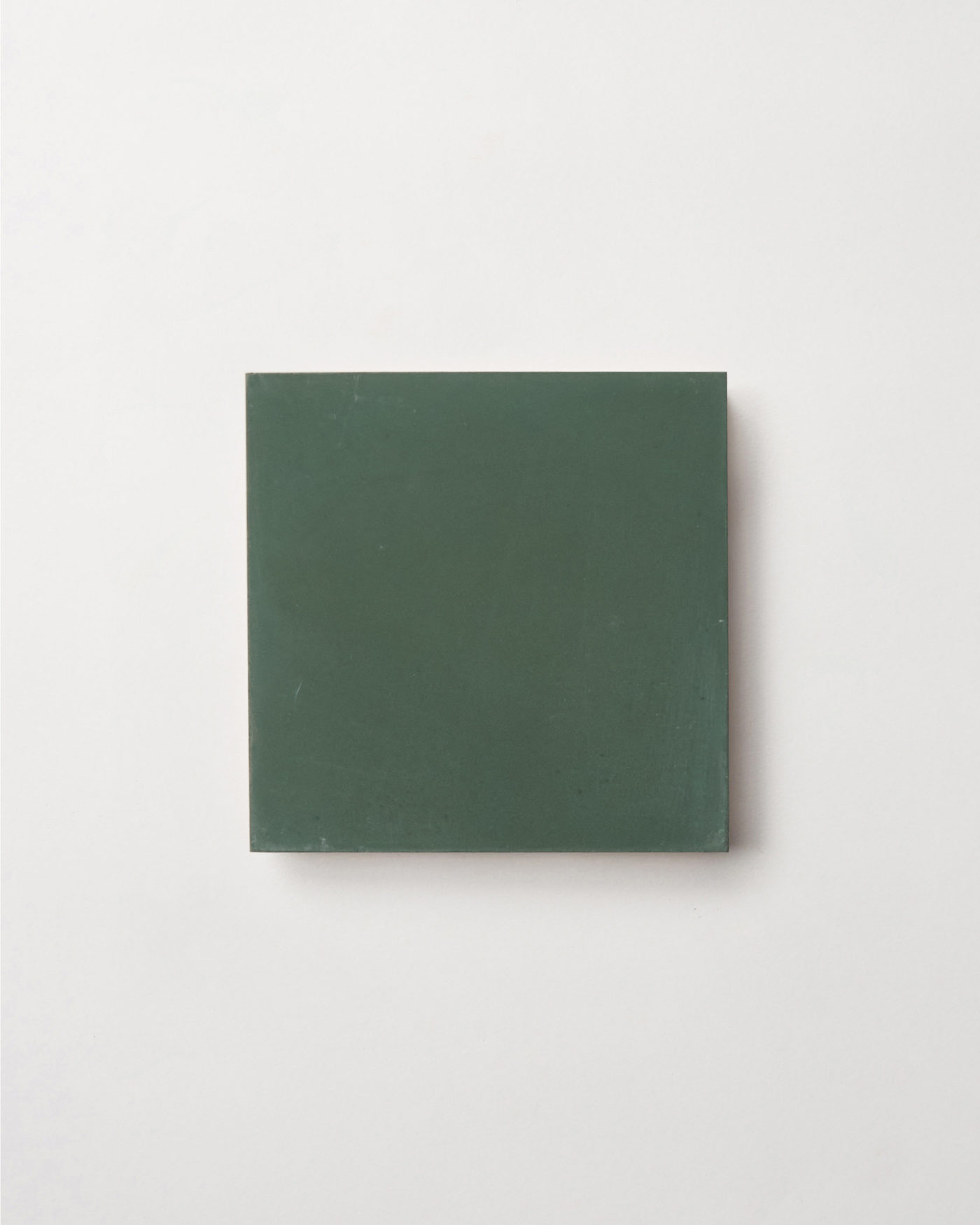 a square piece of green tile on a white surface.