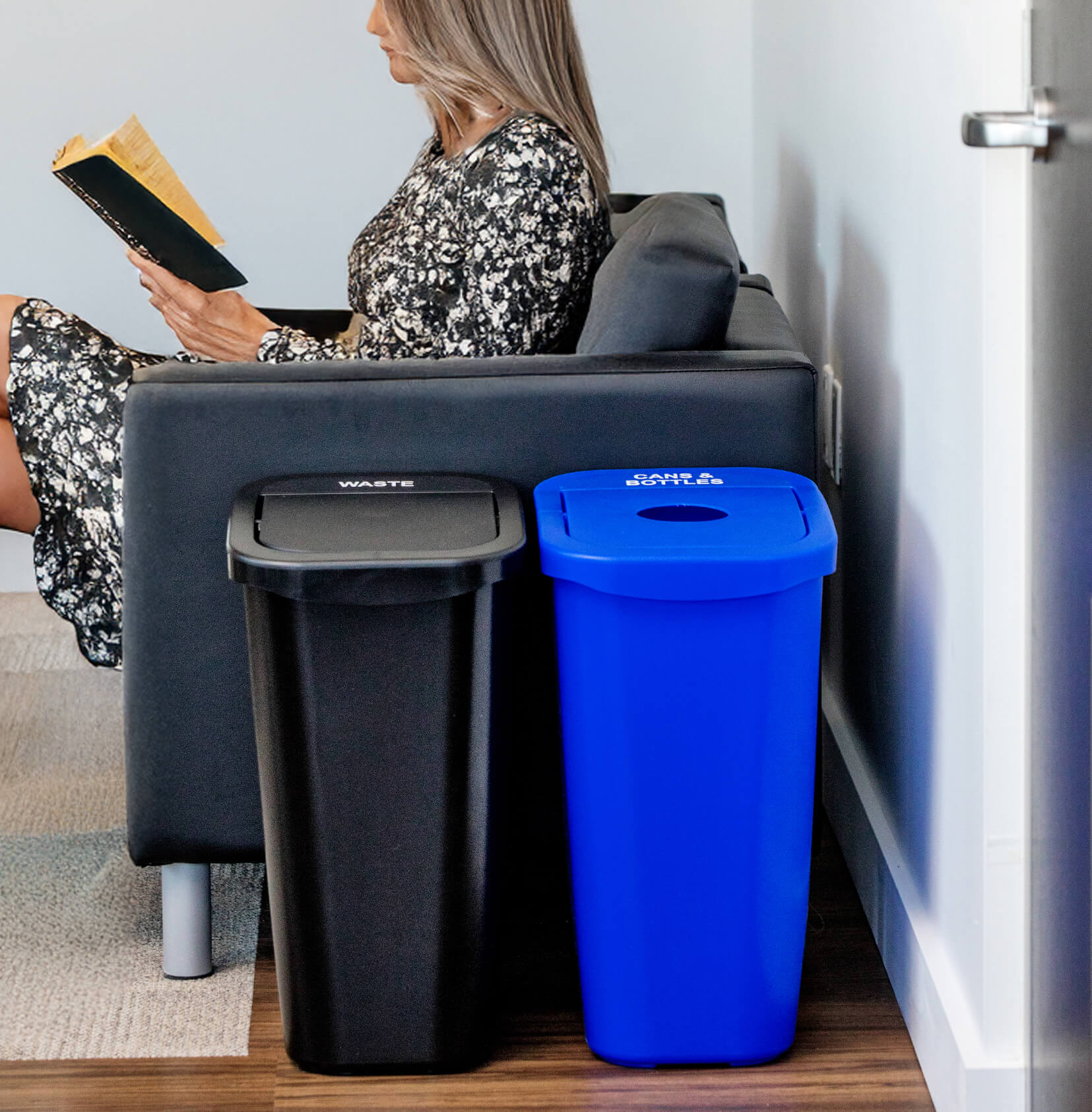 durable plastic waste and recycling containers in a corporate office lounge with a woman sitting in a chair reading a book