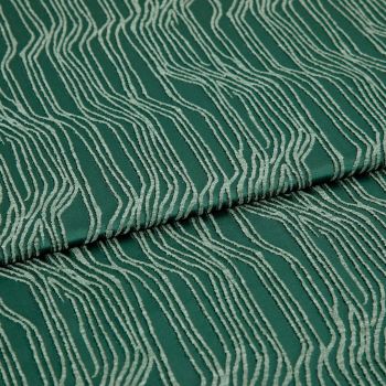 Green jacquard fabric with raised cream wavy lines, folded and overlapping; pattern runs diagonally across a close-up, evenly lit textile surface.