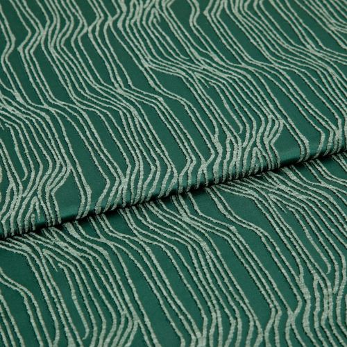 Green jacquard fabric with raised cream wavy lines, folded and overlapping; pattern runs diagonally across a close-up, evenly lit textile surface.