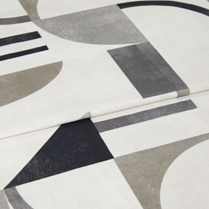 Folded off-white fabric panel with large muted geometric prints (arcs, triangles, rectangles), partially overlapped; appearing as a curtain or textile sample in soft, even indoor light, close-up.
