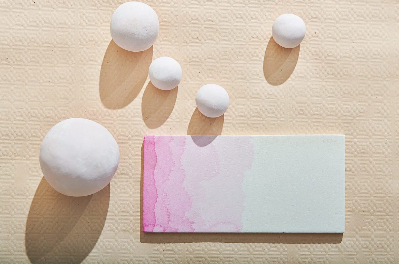 a pink and white patterned tile on a beige surface next to round pieces of ceramic.