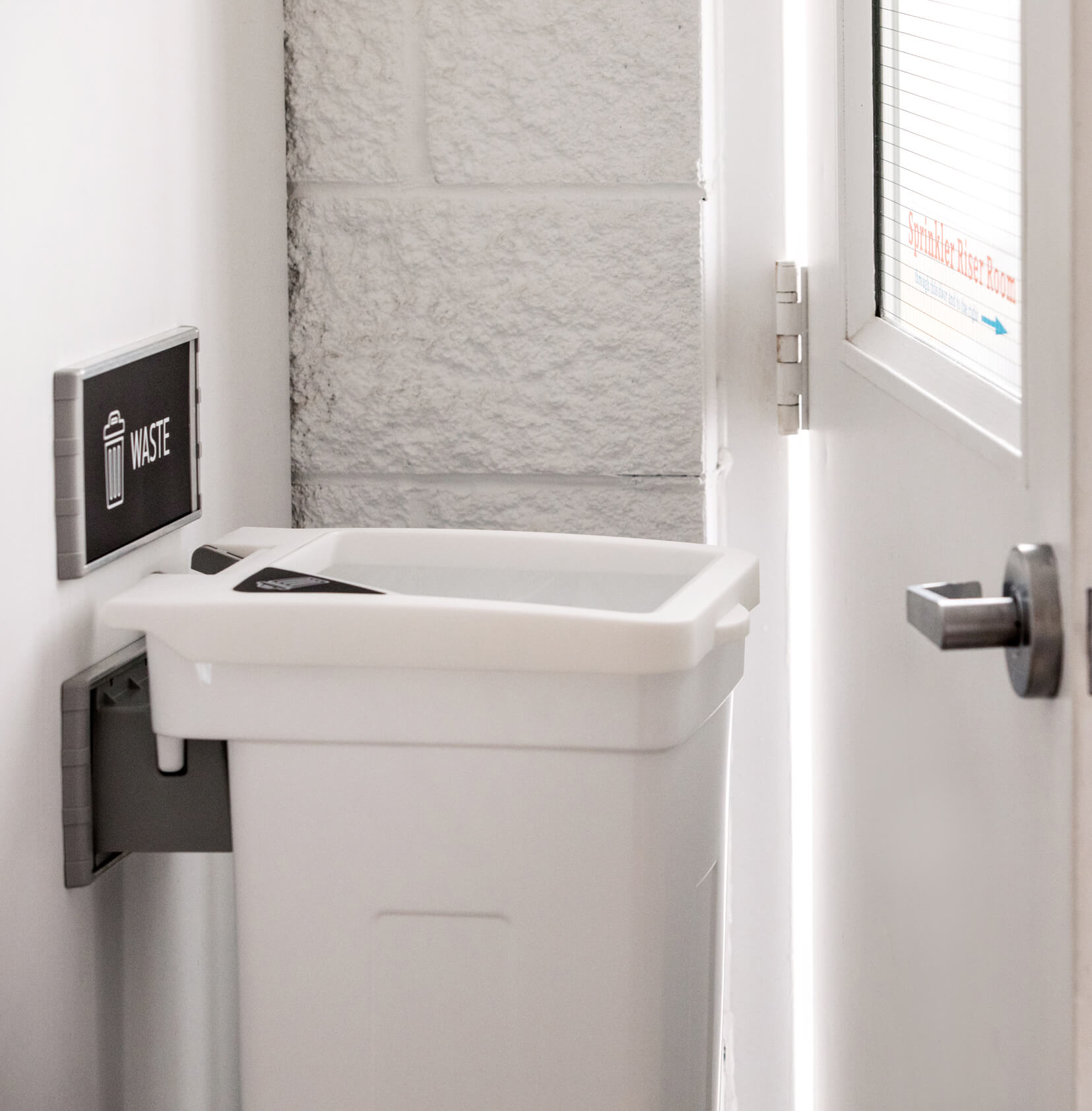 single wall hanging waste container mounted to a wall in a hallway