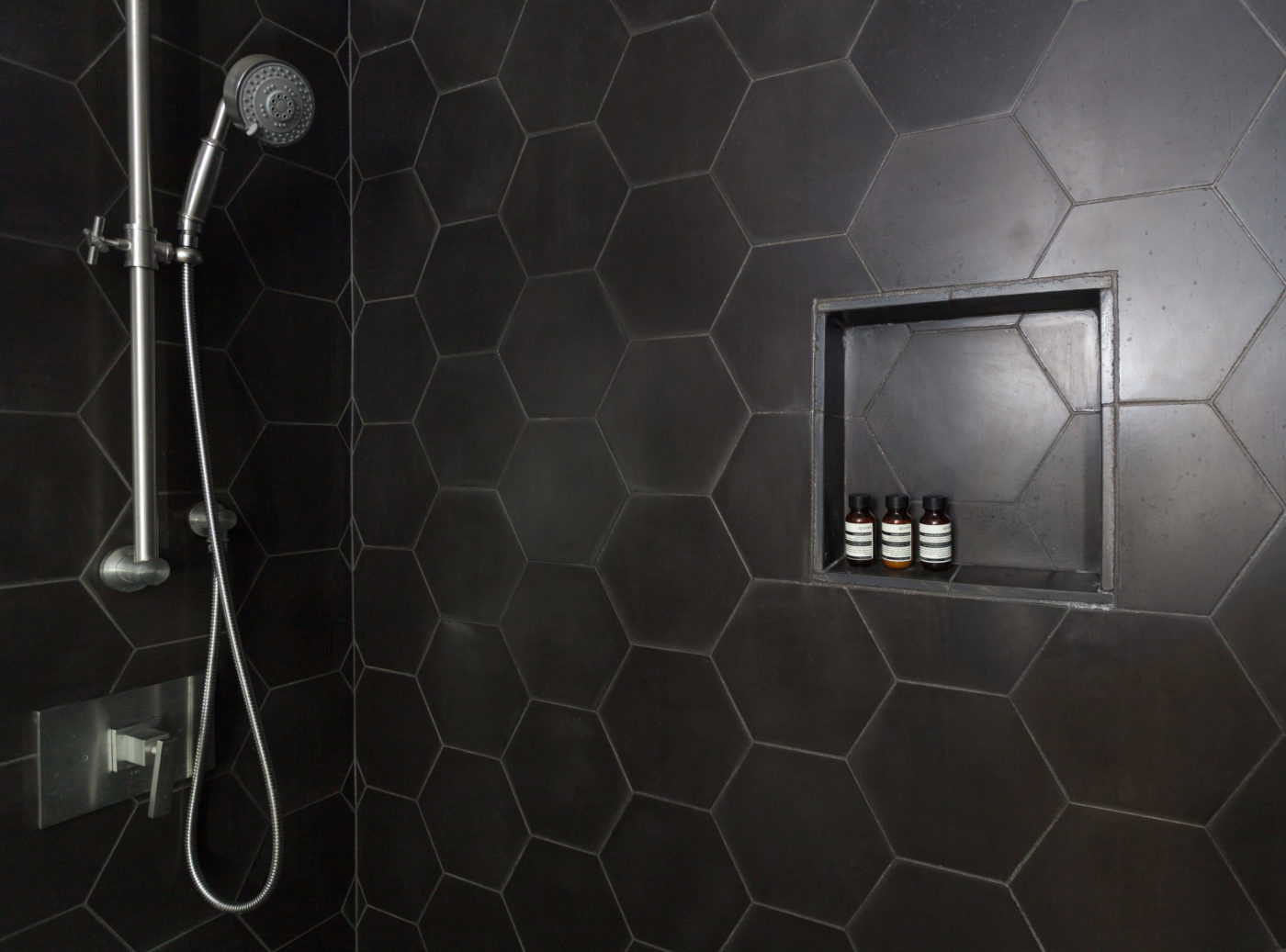 a black hexagon tiled shower with a shower head.